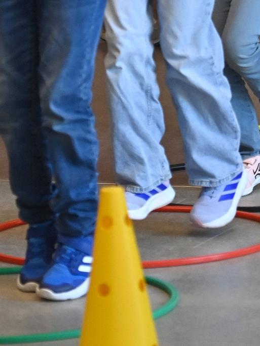 Mehrere Kinderbeine in Turnschuhen während des Sportunterrichts. Sie hüpfen über Reifen, die auf dem Boden liegen. Mehrere Kinderbeine in Turnschuhen während des Sportunterrichts. Sie hüpfen über Reifen, die auf dem Boden liegen.