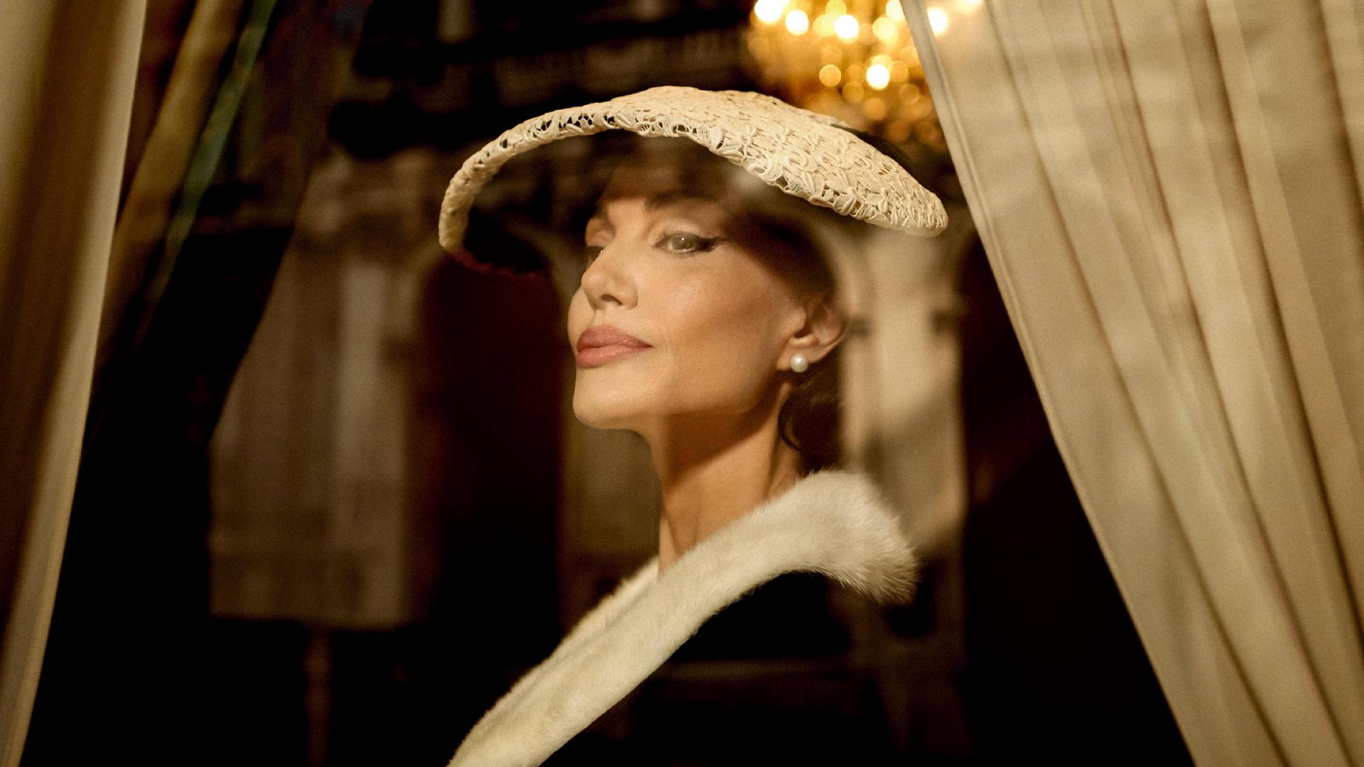 Die US-Schauspielerin Angelina Jolie in der Rolle der Opernsängerin Maria Callas. Sie trägt ein elegantes Kostüm mit Hut im Stil der 1950er-Jahre.
