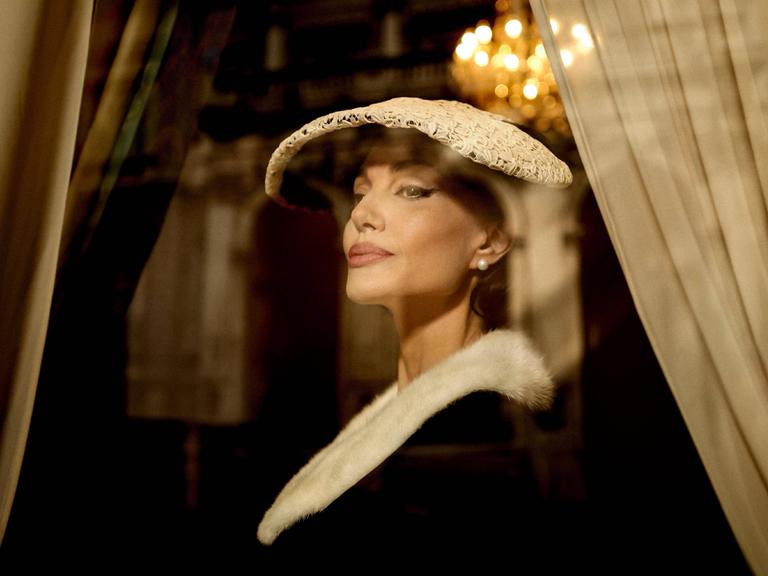 Die US-Schauspielerin Angelina Jolie in der Rolle der Opernsängerin Maria Callas. Sie trägt ein elegantes Kostüm mit Hut im Stil der 1950er-Jahre.
