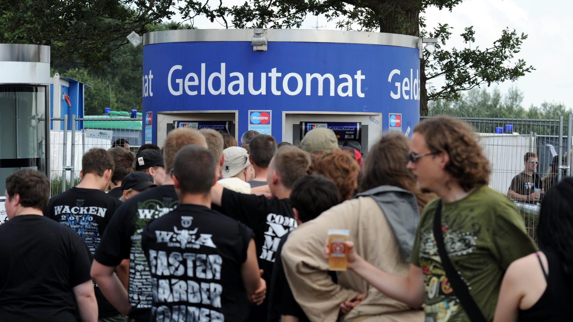 Heavy-Metal-Fans stehen auf dem Gelände des Open-Air-Festivals im schleswig-holsteinischen Wacken vor einem Geldautomaten. 