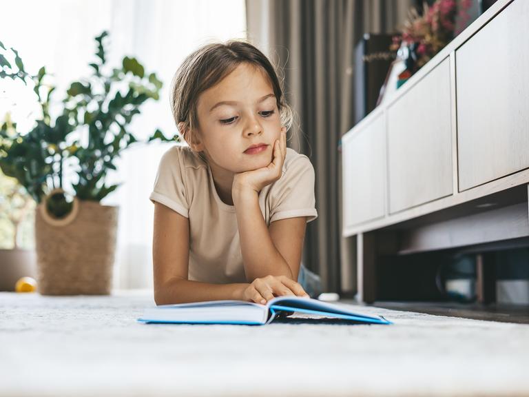 Ein junges Mädchen liegt im Wohnzimmer auf dem Boden und liest ein Buch. Ein junges Mädchen liegt im Wohnzimmer auf dem Boden und liest ein Buch.