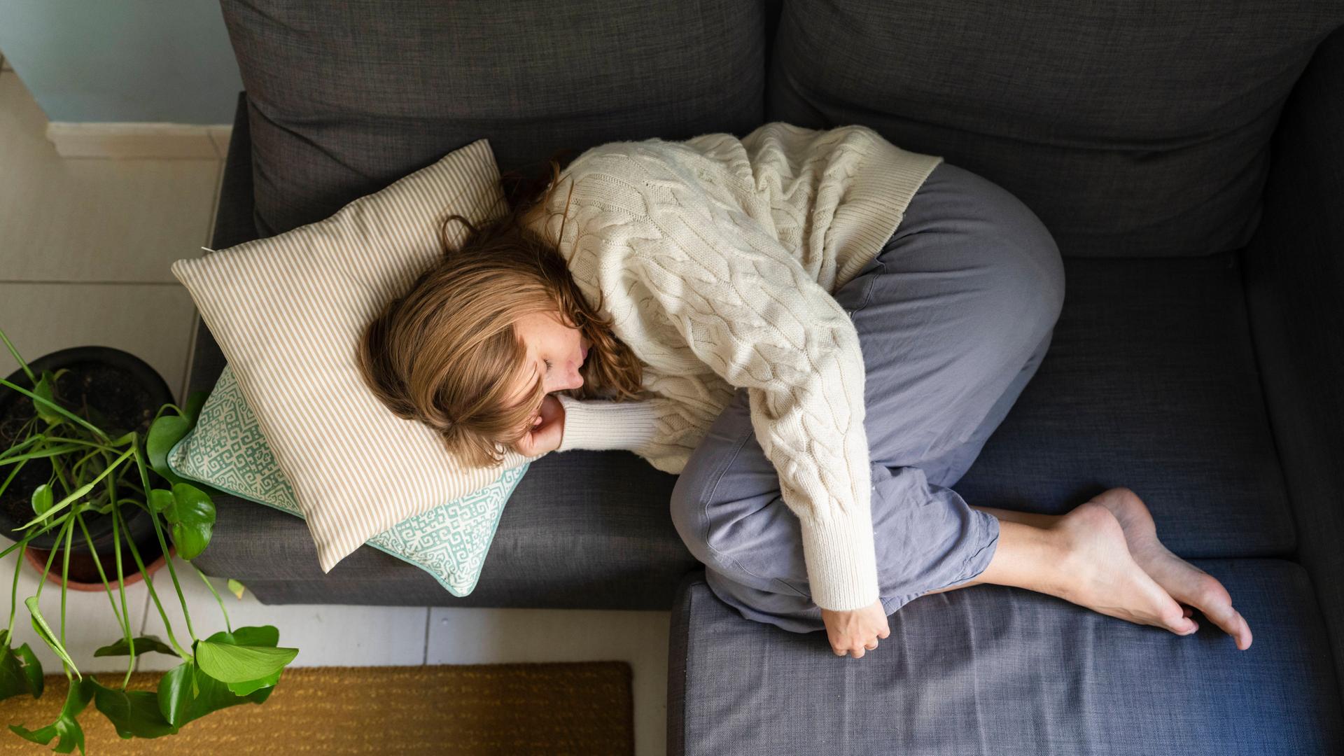 Eine Frau liegt eingerollt auf einem Sofa und hält sich den Bauch.