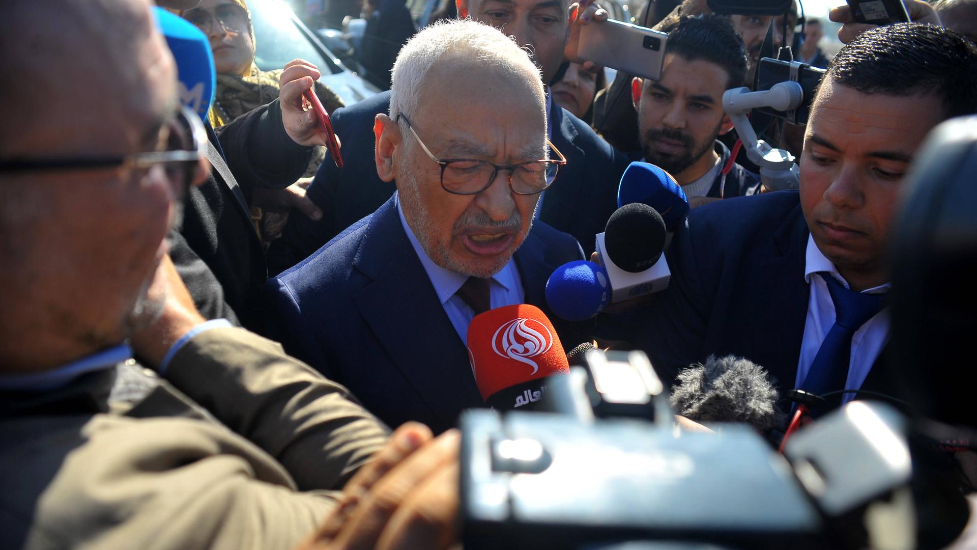 Der Vorsitzende der muslimisch-konservativen Ennahda-Partei, Ghannouchi, ist umringt von Reportern, die ihm Mikrofone entgegenhalten.