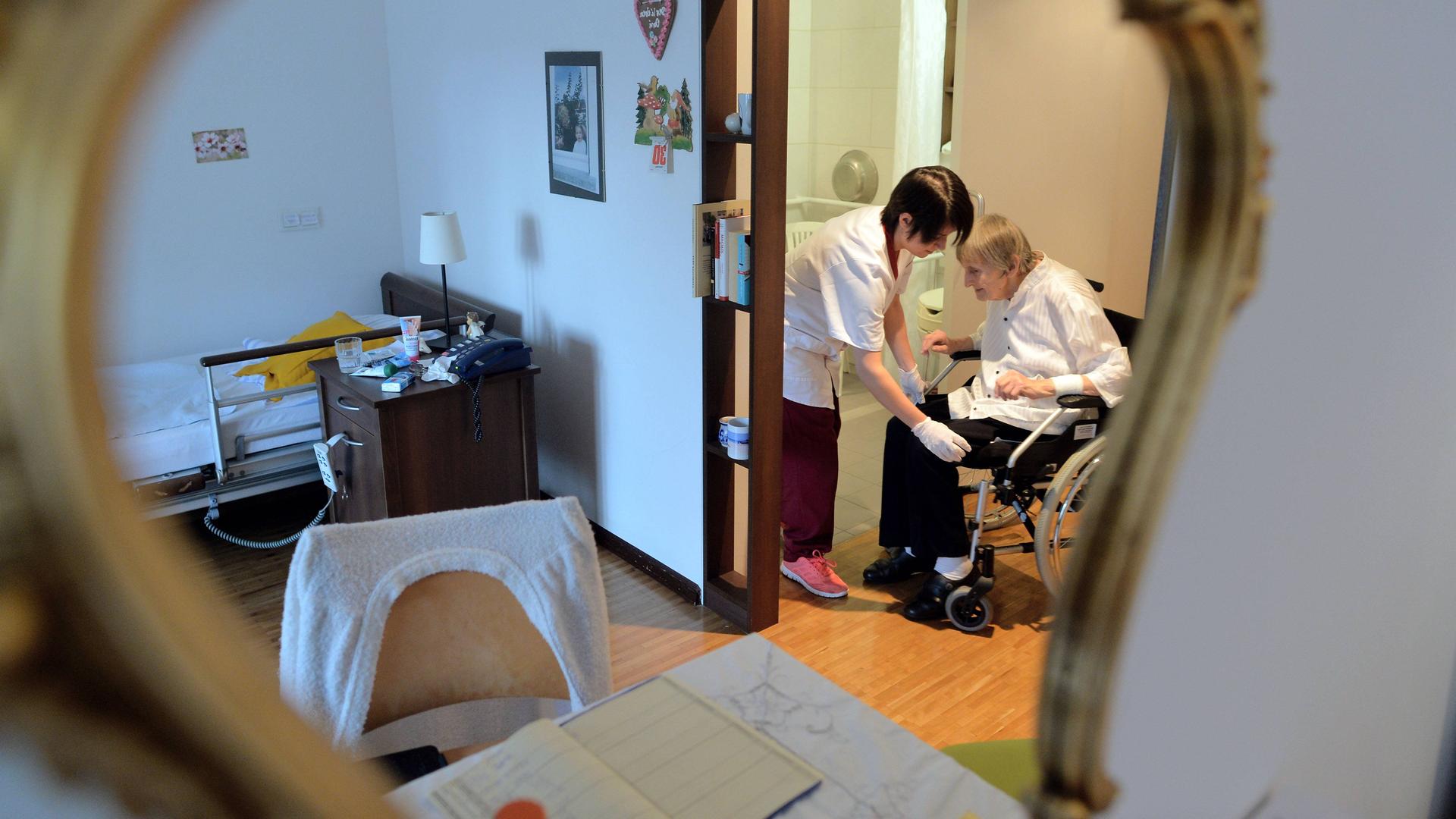 Eine Altenpflegerin versorgt eine im Rollstuhl sitzende Bewohnerin in einem Pflegeheim.