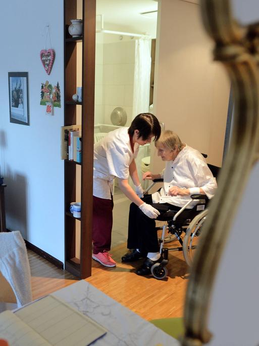Eine Krankenschwester versorgt eine im Rollstuhl sitzende Bewohnerin in einem Pflegeheim.
