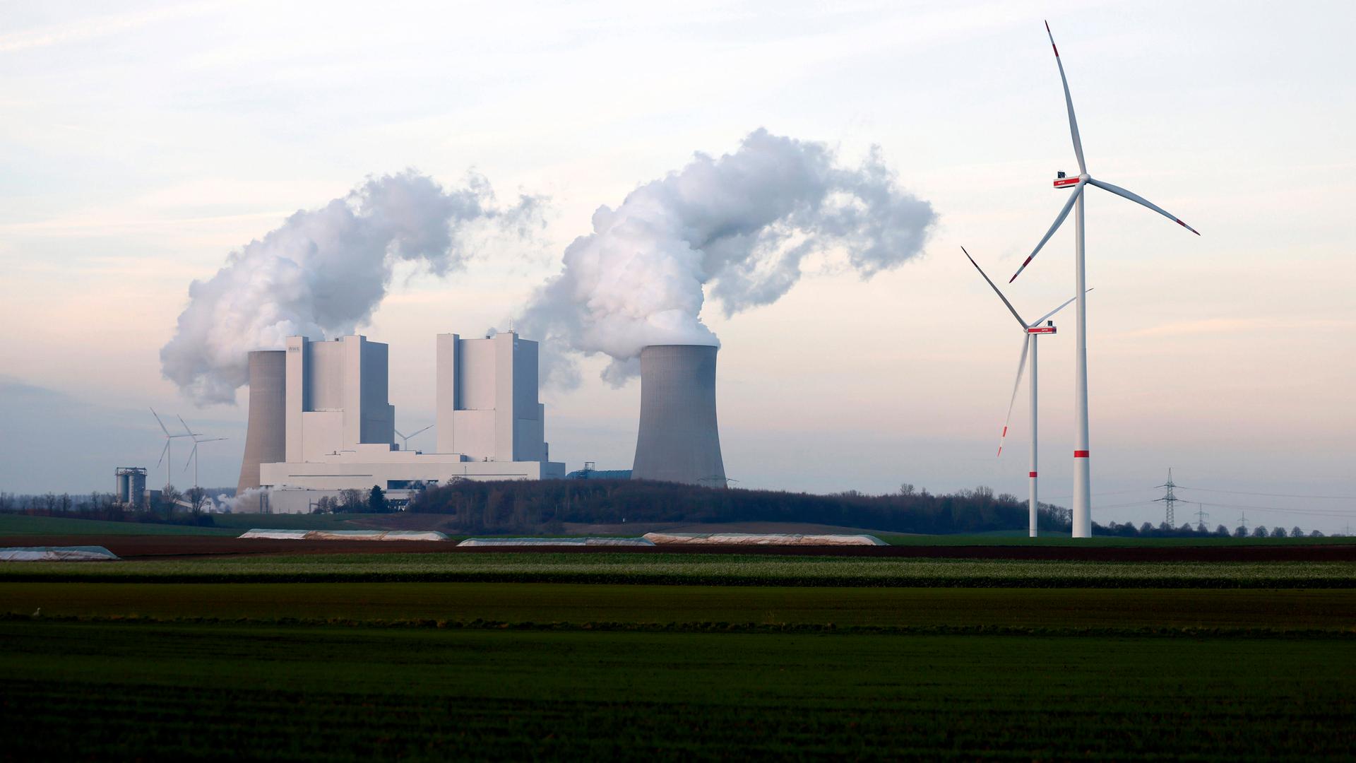 Strommasten und Windräder rund um das Kohlekraftwerk Neurath des Stromkonzerns RWE bei Grevenbroich. Aus den Kühltürmen steigen dicke Dampfwolken in den Himmel.  