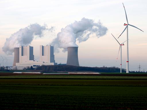 Strommasten und Windräder rund um das Kohlekraftwerk Neurath des Stromkonzerns RWE bei Grevenbroich. Aus den Kühltürmen steigen dicke Dampfwolken in den Himmel.  