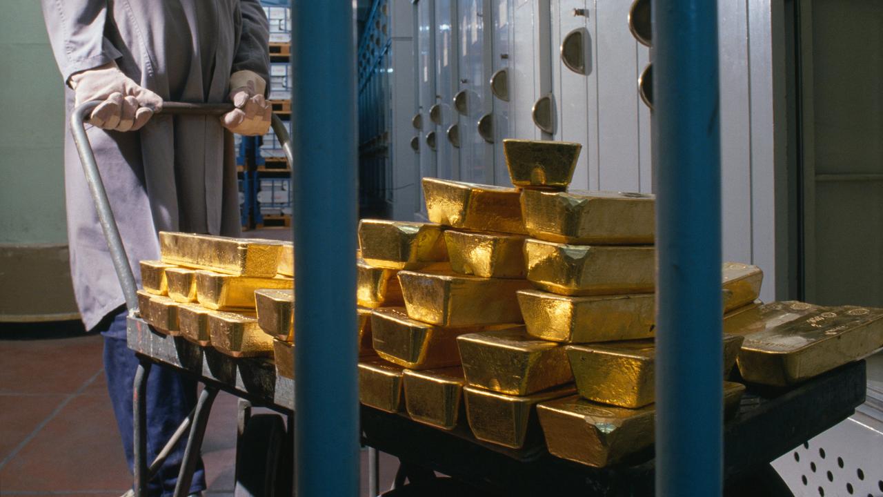 Gestapelte Goldbarren der "Banque de France" werden im Jahr 1989 von einem Bankmitarbeiter mit Handschuhen und grauem Arbeitskittel auf einem Karren hinter Gittern geschoben. Im Hintergrund stehen viele Metallschränke und Regale.