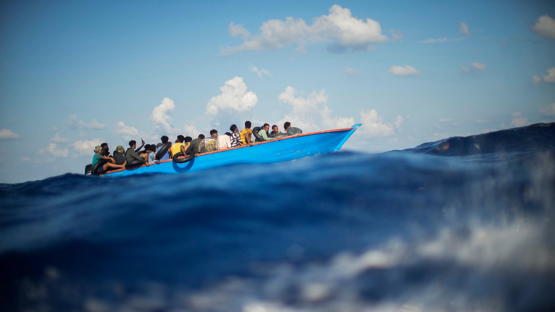 Migranten sitzen in einem Holzboot im Mittelmeer. 