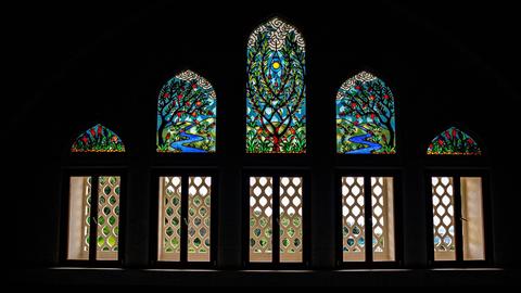 Blick über einen orientalischen Teppich zu einer bunten Fensterfront, die mit buntem Glas einen Ausblick auf einen Garten suggeriert.