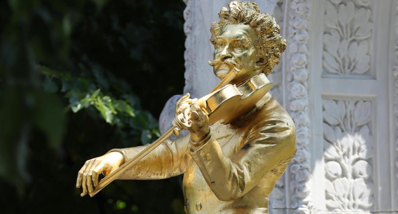 Blick auf die goldene Figur des Johann Strauss Sohn-Denkmals in Wien, bei dem der Komponist mit markantem Schnurrbart eine Geige spielt.