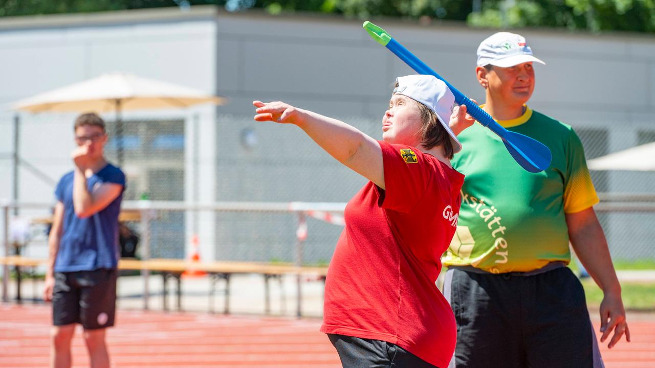 Eine Frau wirft einen Speer, hinter ihr steht ein Mann. Beide tragen Sportkleidung.