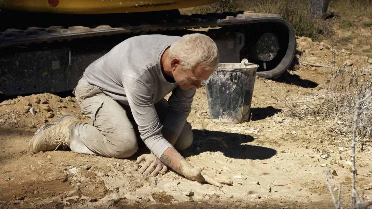 Der britische Naturkünstler Andy Goldsworthy bei einem seiner Projekte am Boden kniend und mit den Hängen im Matsch arbeitend