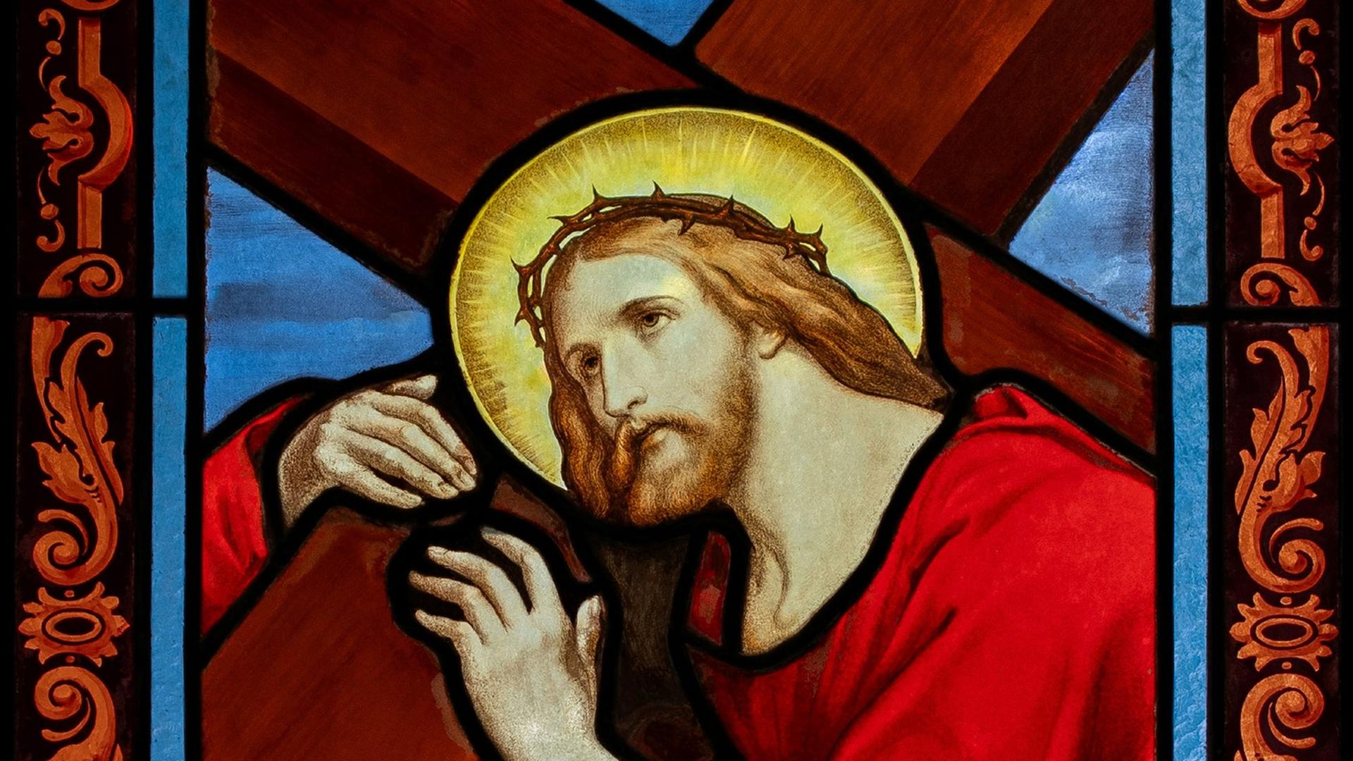 Kirchenfenster, das Jesu mit roter Kleidung und Heiligenschein das Kreuz tragend zeigt.