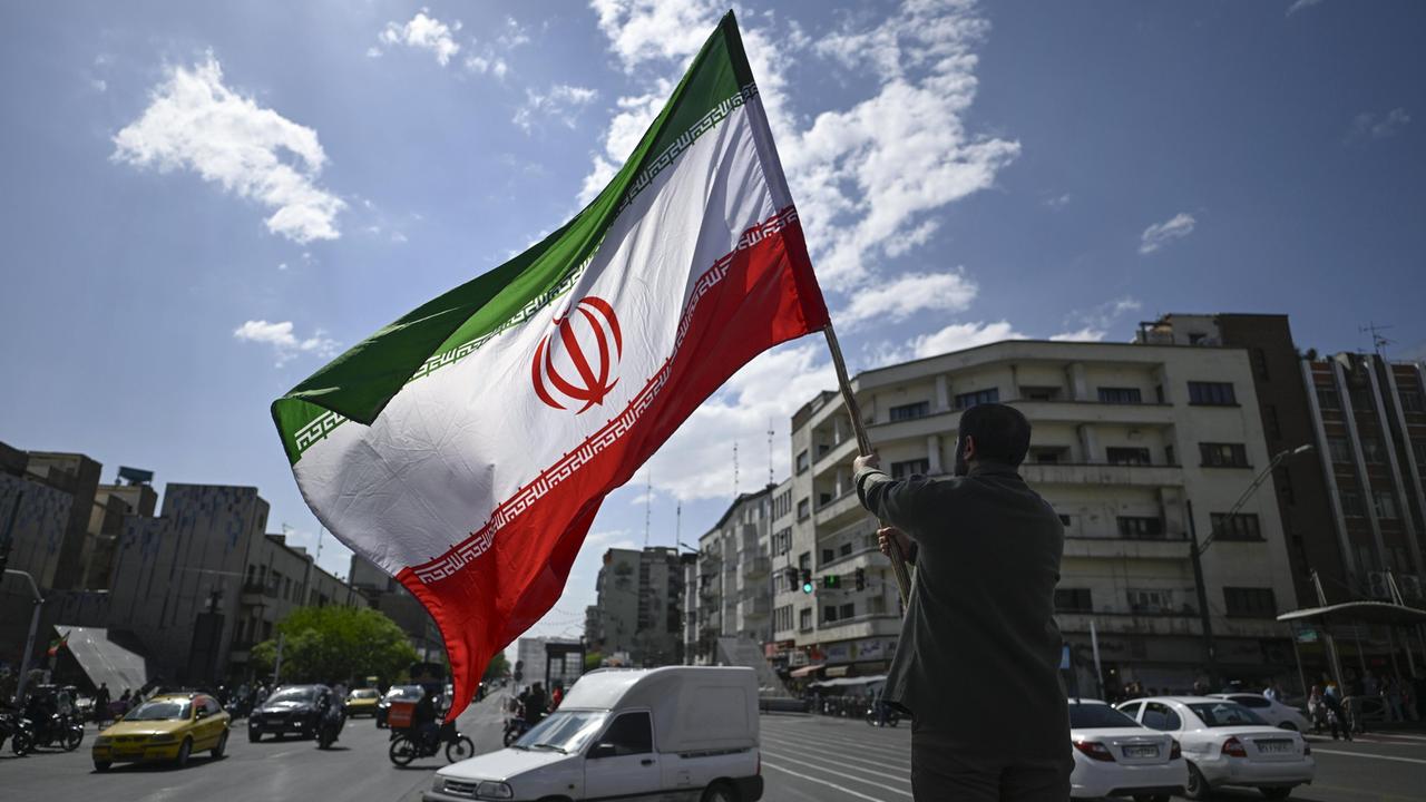 In Teheran hält ein Mann eine iranische Flagge in die Höhe.
