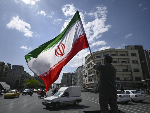 In Teheran hält ein Mann eine iranische Flagge in die Höhe.