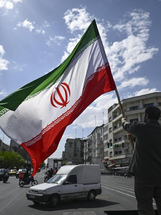 In Teheran hält ein Mann eine iranische Flagge in die Höhe.