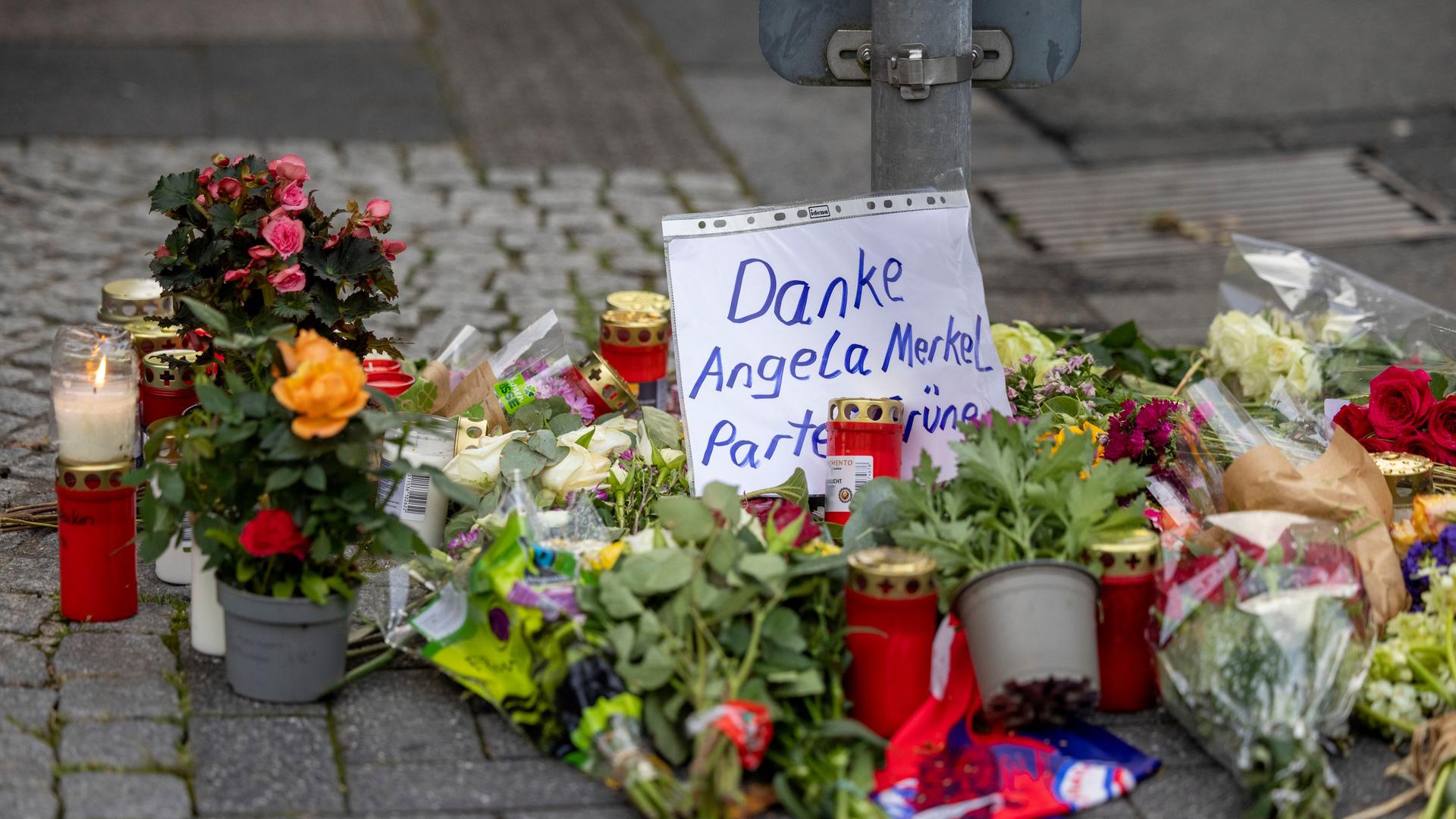 Inmitten eines Blumengestecks zum Gedenken an die Opfer von Solingen steht ein Schild mit der Aufschrift: "Danke Angela Merkel Partei Grüne".