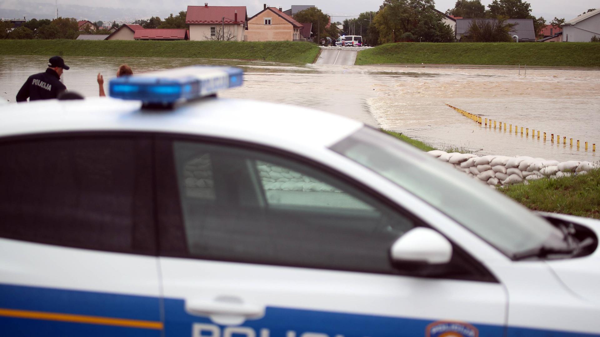 Ein Polizeiauto steht in Slowenien an einem überschwemmten Fluss.