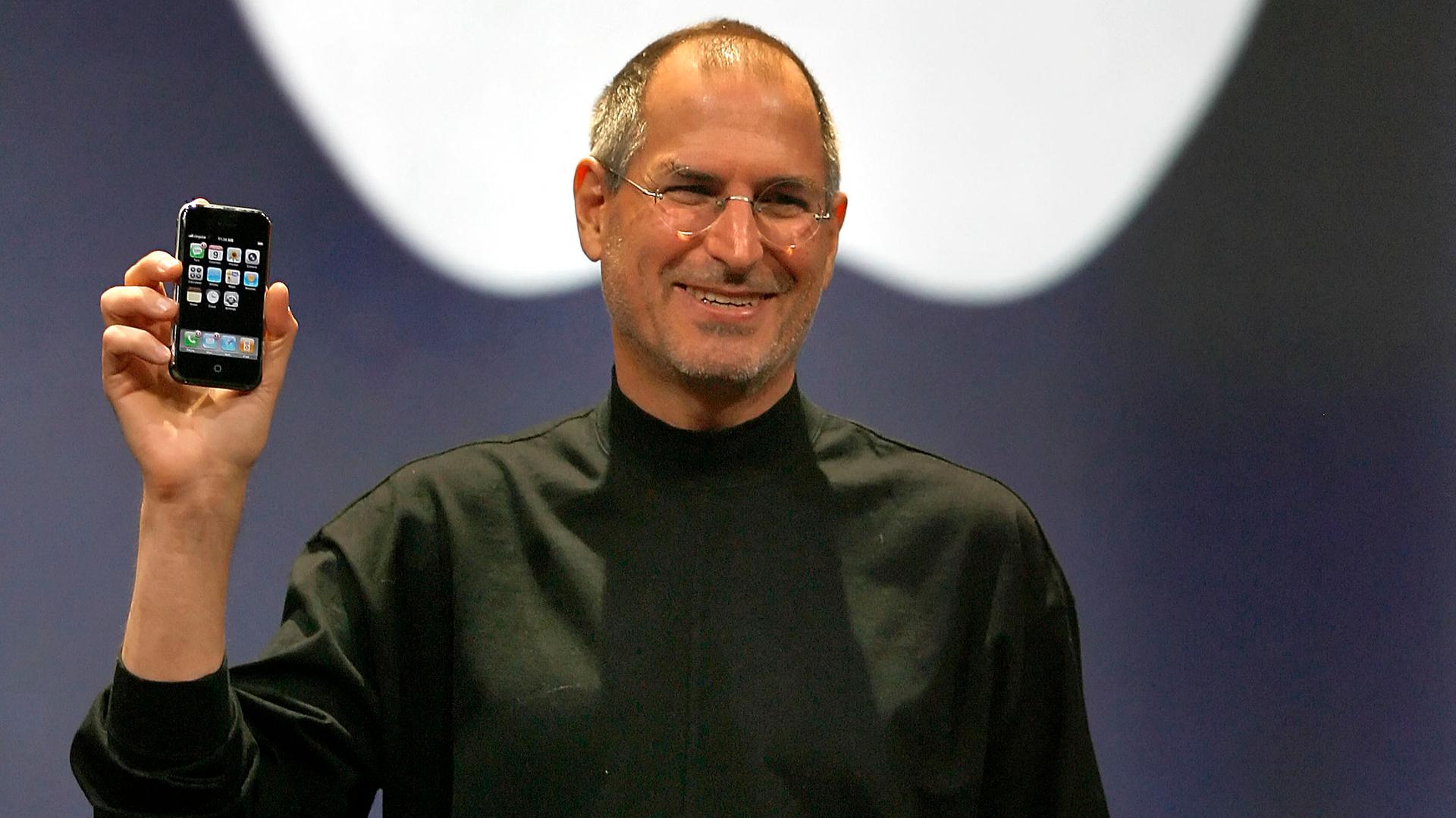 Der frühere Apple-Chef Steve Jobs hält 2007 vor dem Logo der Firma ein neues Mobiltelefon hoch, das erste „iPhone“ Der frühere Apple-Chef Steve Jobs hält 2007 vor dem Logo der Firma ein neues Mobiltelefon hoch, das erste „iPhone“