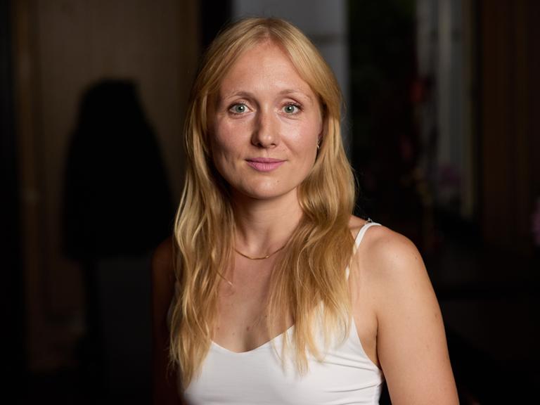 Die Autorin Ruth-Maria Thomas steht in einem weißen Oberteil vor dunklem Hintergrund. Die Autorin Ruth-Maria Thomas steht in einem weißen Oberteil vor dunklem Hintergrund.