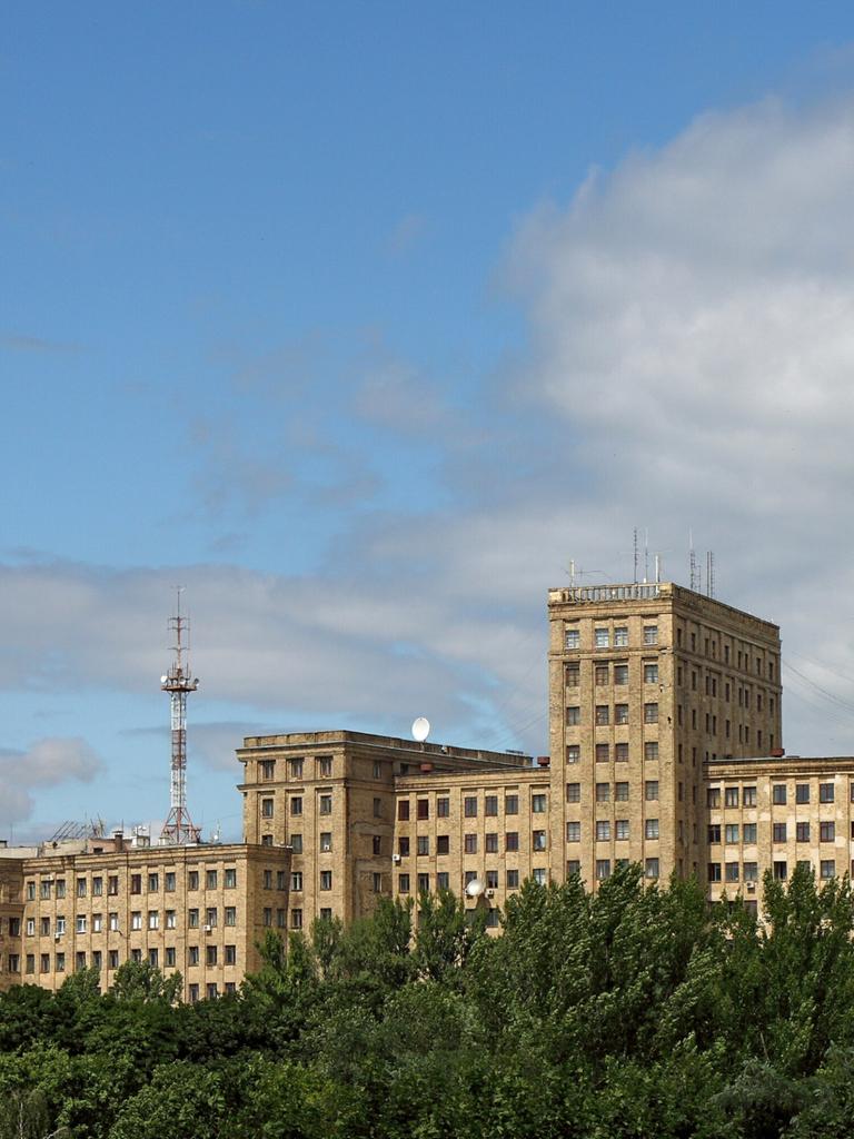 Das langgestreckte Universitätsgebäude von Charkiw erhebt sich über einem grünen Laubwald vor strahlend blauem Himmel.