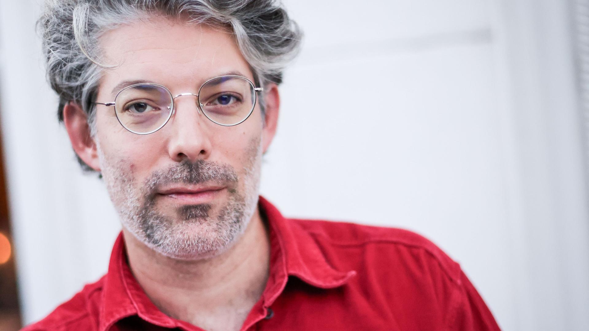 Der Autor Tomer Dotan-Dreyfus steht in rotem Hemd vor einer weißen Wand mit einem Fenster