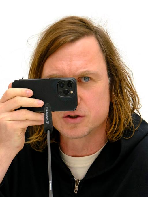 Der Schauspieler Lars Eidinger hält sein Handy vor das Gesicht bei der Pressekonferenz zu seiner Fotoausstellung mit dem Titel "O Mensch" im K21 der Stiftung Kunstsammlung Nordrhein-Westfalen in Düsseldorf.