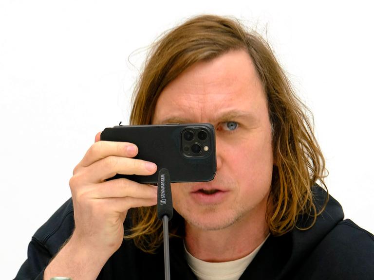 Der Schauspieler Lars Eidinger hält sein Handy vor das Gesicht bei der Pressekonferenz zu seiner Fotoausstellung mit dem Titel "O Mensch" im K21 der Stiftung Kunstsammlung Nordrhein-Westfalen in Düsseldorf.