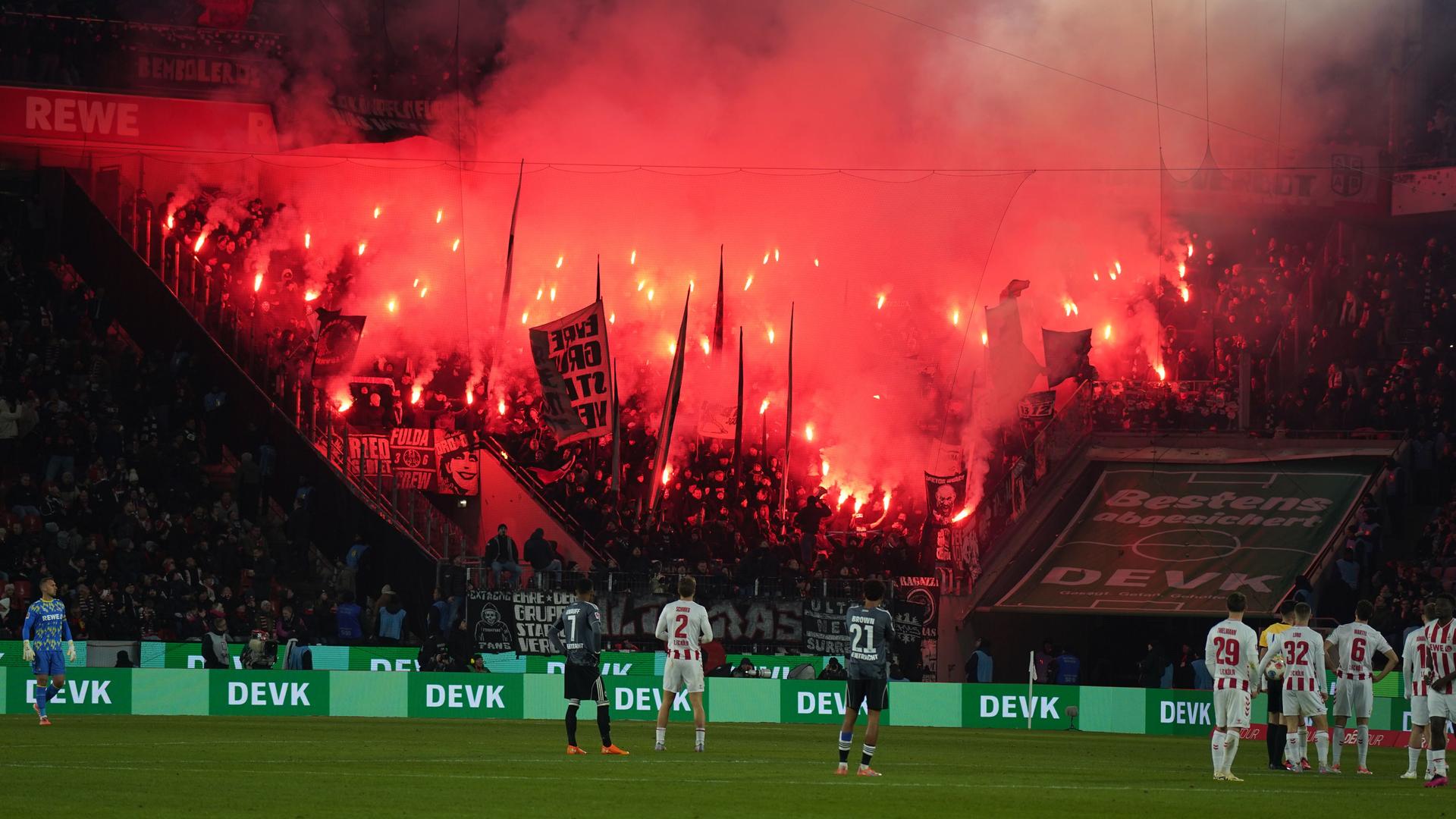 Es ist dunkel. Blick auf den Block der Eintracht-Fans, der rot leuchtet und raucht. Auf dem Rasen stehen Spieler und schauen hoch. 