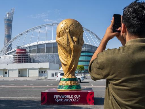 Ein Mann macht ein Foto von einem übergroßem WM-Pokal der vor dem Khalifa Stadium in Doha steht.
