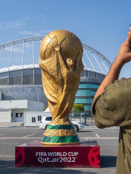 Ein Mann macht ein Foto von einem übergroßem WM-Pokal der vor dem Khalifa Stadium in Doha steht.