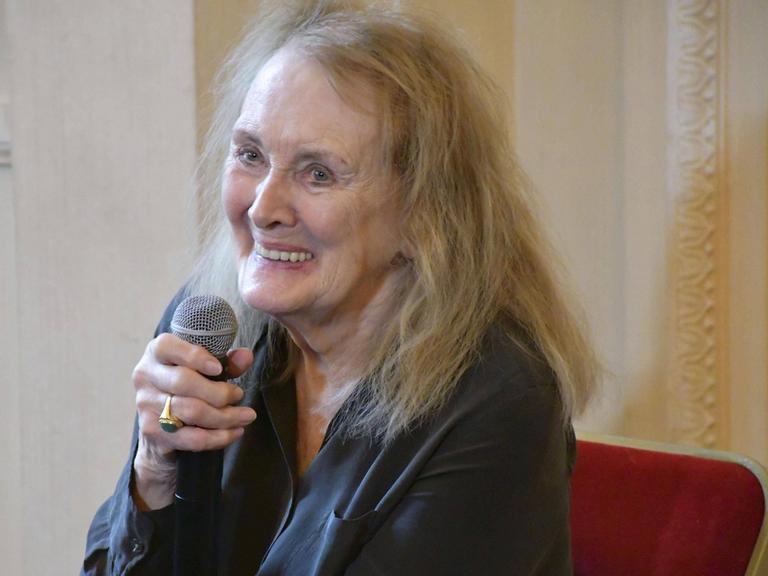 Annie Ernaux sitz an einem Tisch und hält ein Mikrofon in der Hand