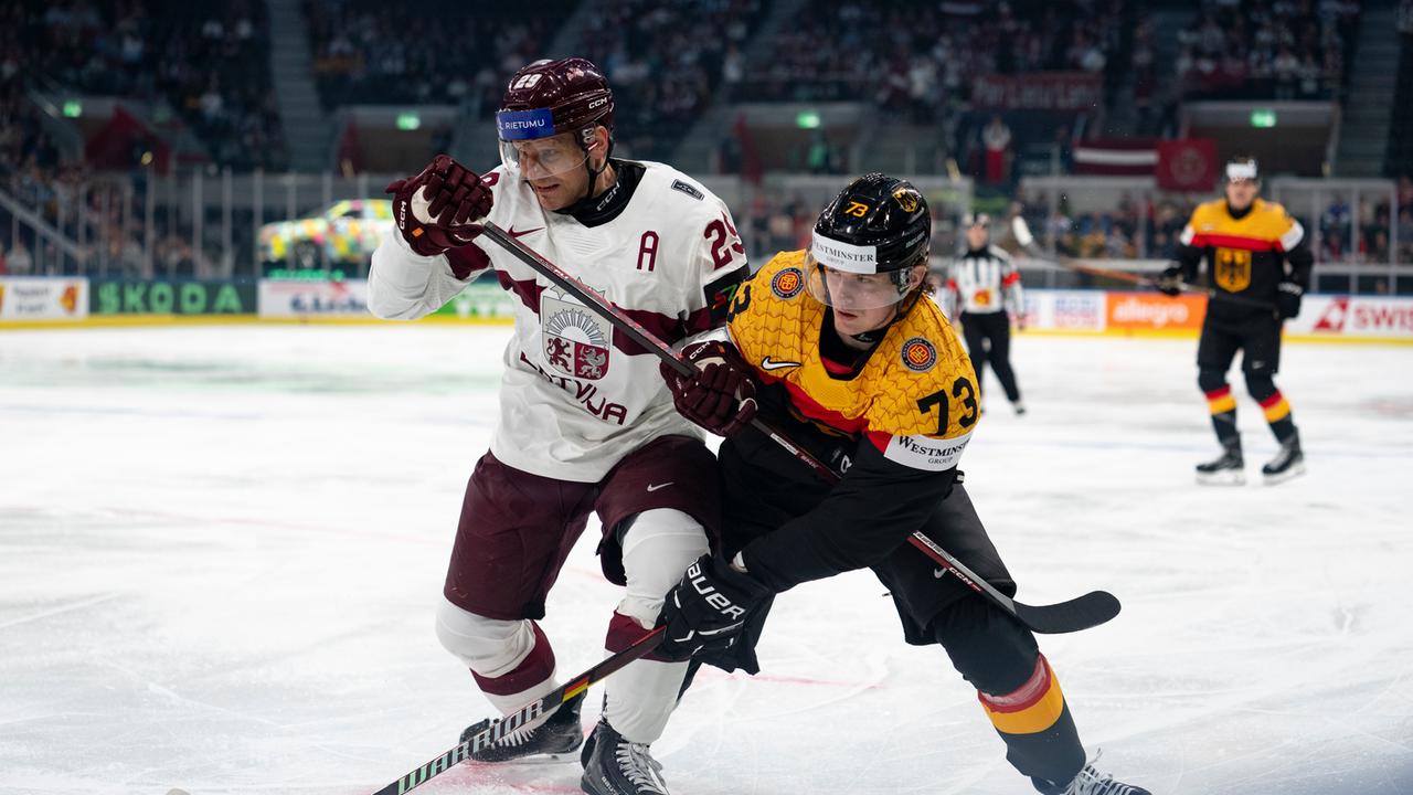 Der lettische Nationalspieler Ralfs Freibergs (links) in Aktion gegen Lukas Reichel von der deutschen Auswahl. Beide rangeln heftig um den Puck.