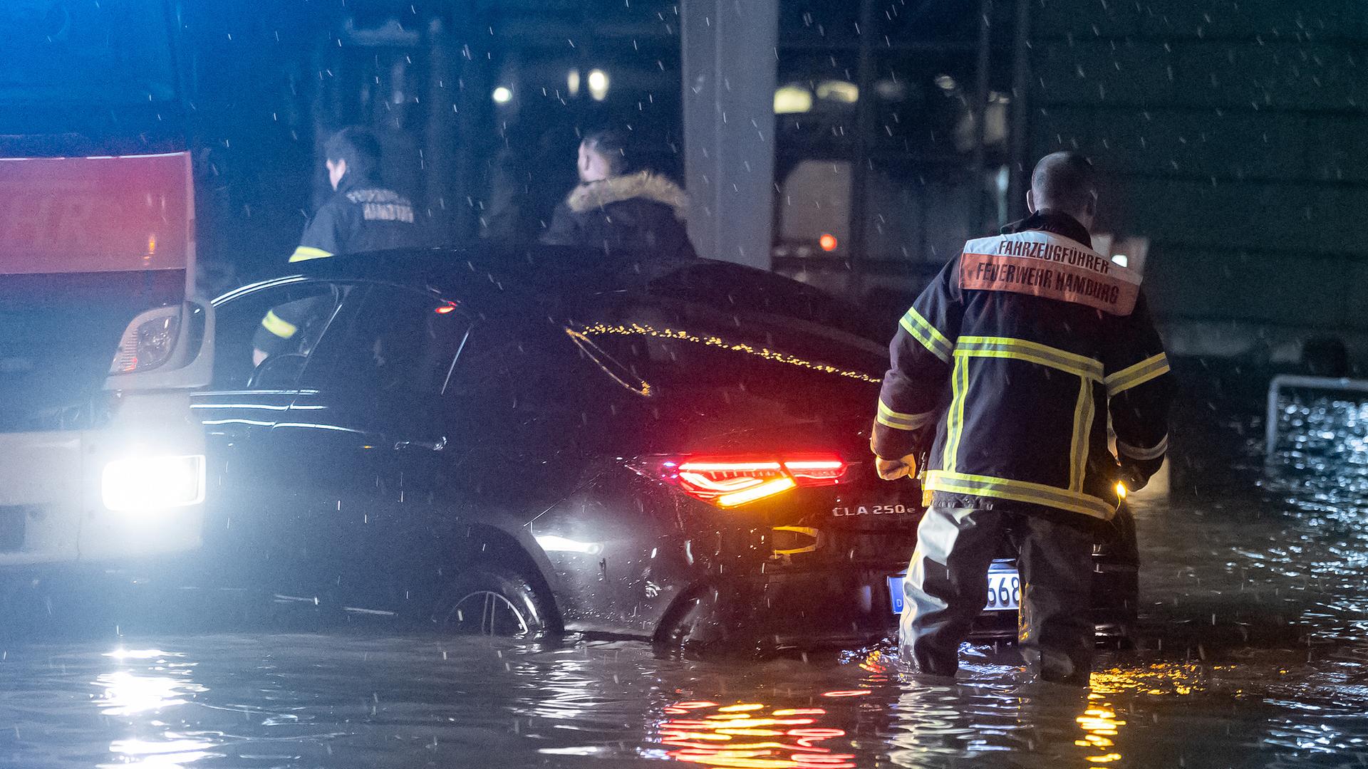 Ein PKW steht bei einer Sturmflut in der Nähe des Fischmarkts im Wasser der Elbe. Einsatzkräfte der Feuerwehr leisten Hilfestellungen.