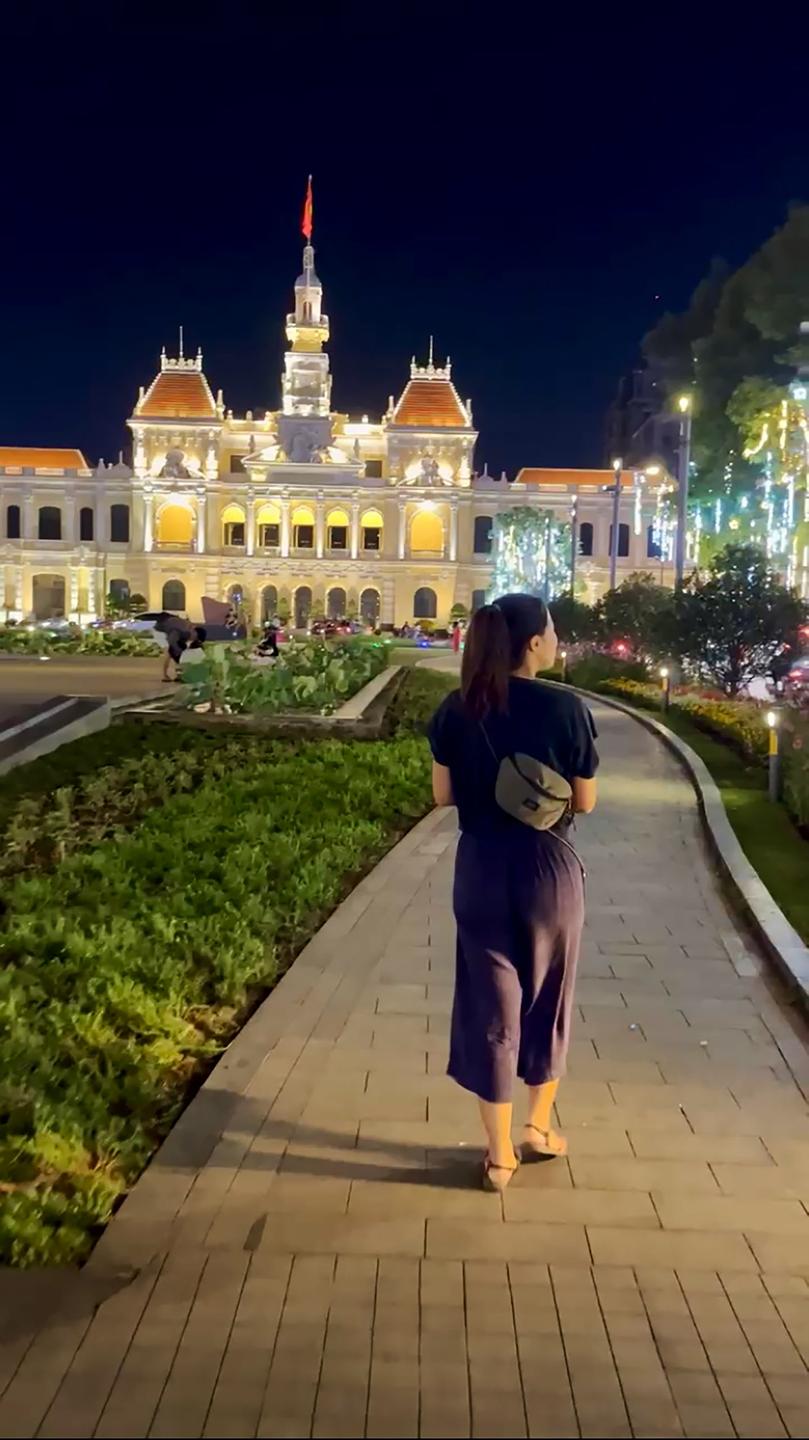 Eine junge Frau spaziert im Vorgarten des Rathauses in Ho-Chi-Minh-Stadt. Das Haus ist ein kolonialer Prunkbau und nächtlich beleuchtet. Eine junge Frau spaziert im Vorgarten des Rathauses in Ho-Chi-Minh-Stadt. Das Haus ist ein kolonialer Prunkbau und nächtlich beleuchtet.