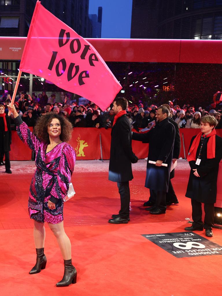 Schauspielerin Denise M'Baye steht mit einer pinken Flagge mit der Aufschrift "vote love" am Eröffnungsabend der Berlinale auf dem verschneiten Roten Teppich.