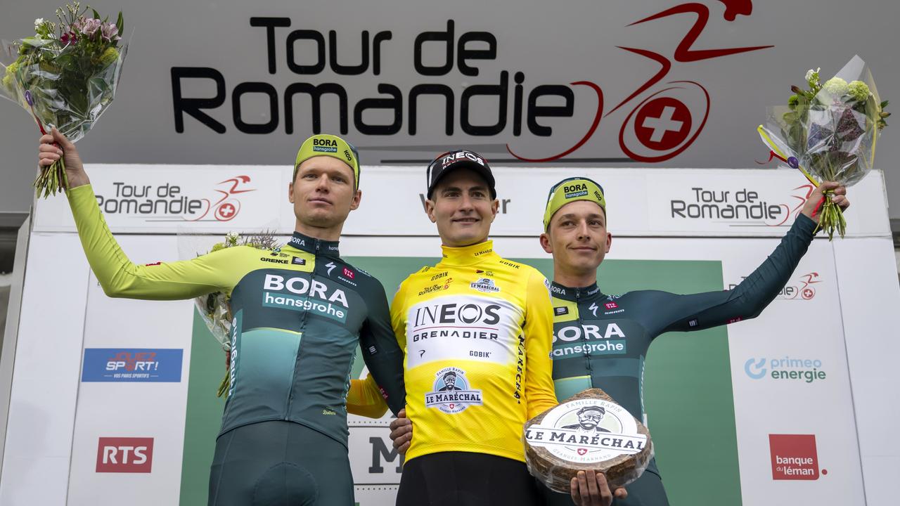 Drei Radrennfahrer stehen auf dem Podium und feiern ihren Sieg.