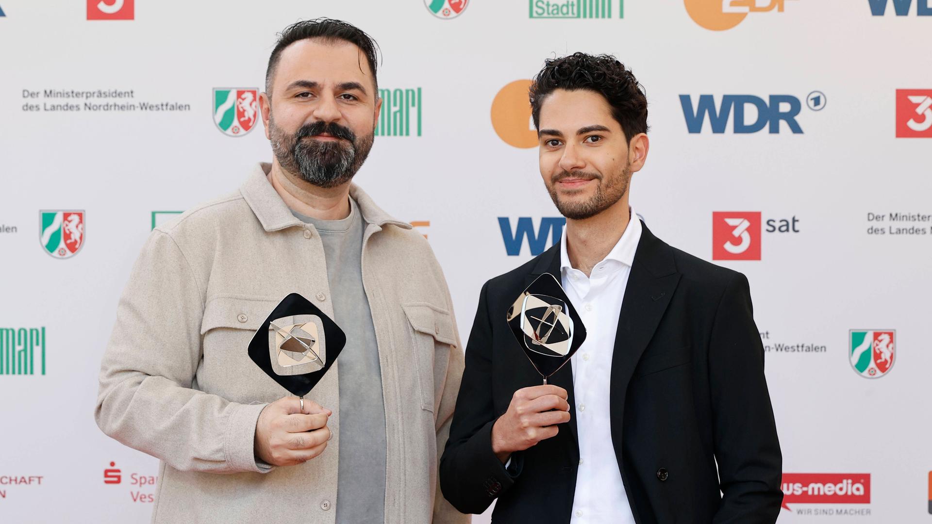 Bilal Bahadir und Cagdas Eren Yüksel bei der Verleihung des Grimme Preises. Beide haben eine Trophäe in den Händen und lächeln in die Kamera.