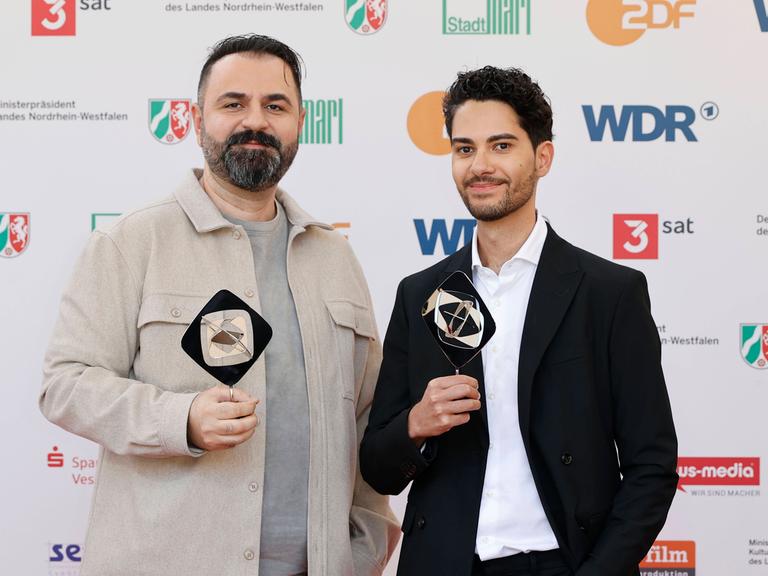 Bilal Bahadir und Cagdas Eren Yüksel bei der Verleihung des Grimme Preises. Beide haben eine Trophäe in den Händen und lächeln in die Kamera.