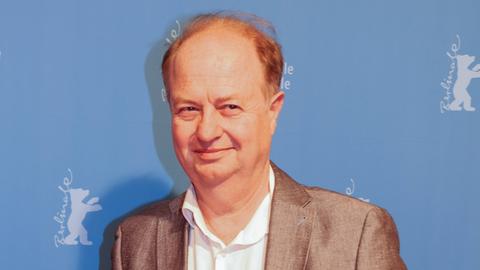 Christoph Jungmann posiert lächelnd bei der Berlinale für die Fotografen. Er trägt ein weißes Hemd und ein hellbraunes, glänzendes Sakko.