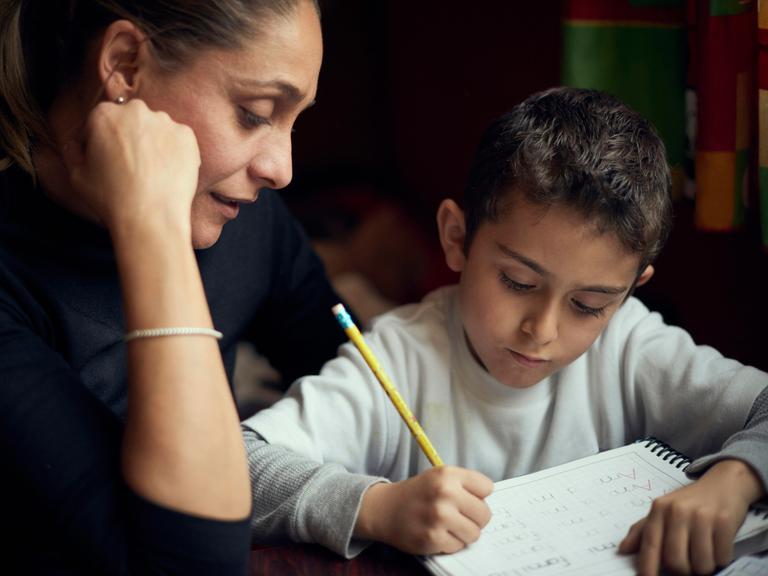 Eine Mutter beobachtet ihren Sohn beim Schreiben des Alphabets.