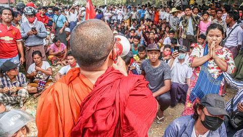Ein buddhistischer Mönch in Myanmar spricht zu einer Menschenmenge.