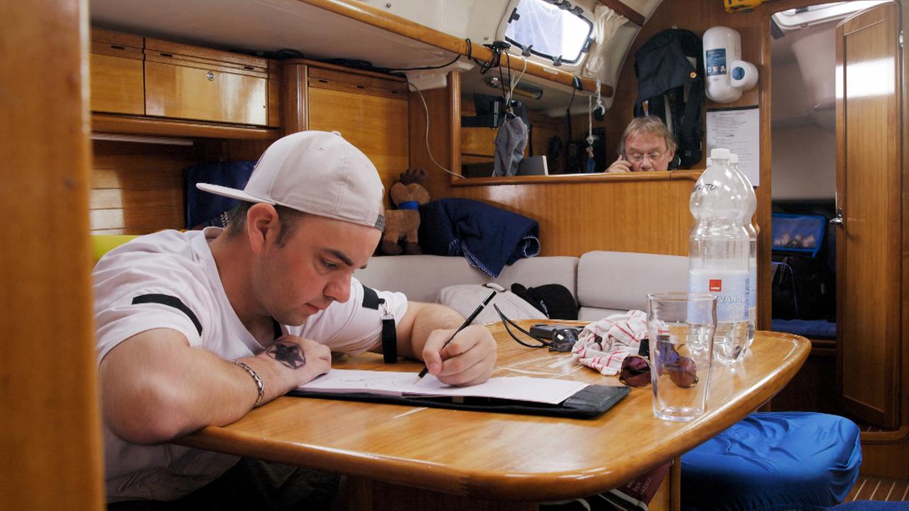 Ein junger Mann mit Baseballkappe beugt sich mit einem Bleistift in der Hand über einen Zeichenblock.