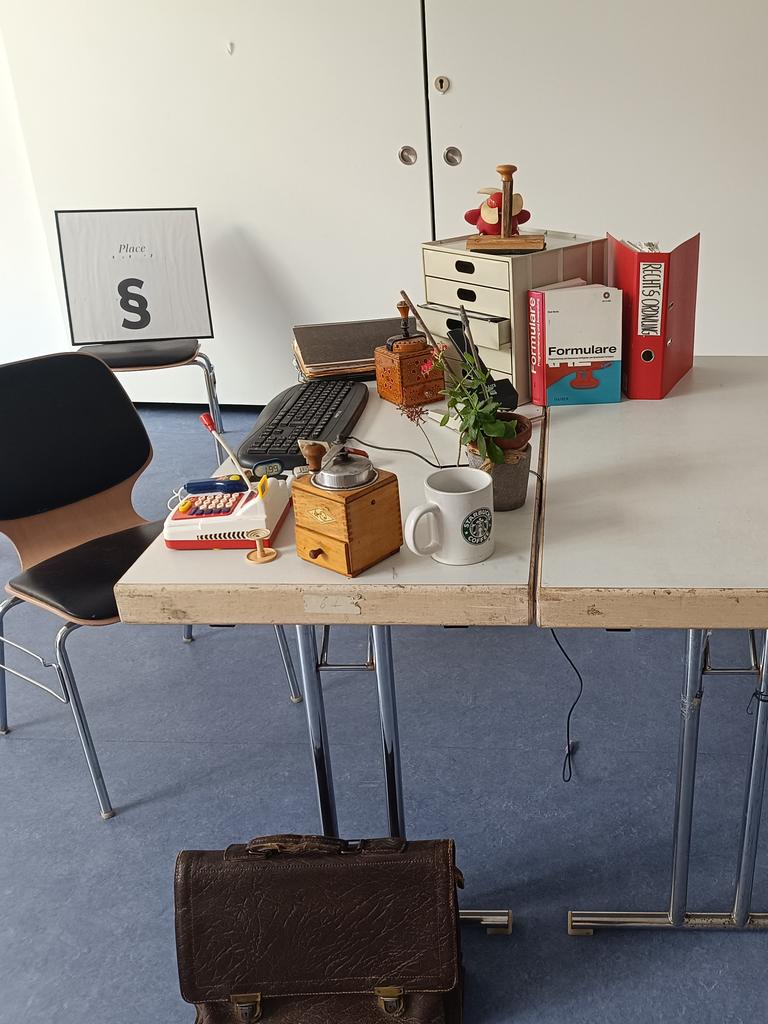 Bühnenbild aus dem Stück "Der Paragraphenreiter" vom "Theater der Verrückten" in Berlin Neukölln. Zu sehen ist ein voll gestellter Schreibtisch mit Aktenordner, Kaffemühle, Keyboard und weiteren amtstypischen Objekten