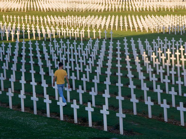 Ein Mann geht entlang weißer Kreuze über die Gedenkstätte Verdun, Schlachtfeld des Ersten Weltkrieg