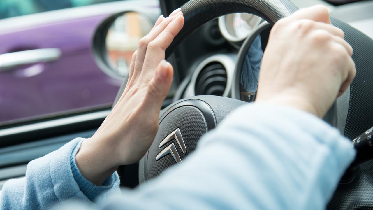 Eine junge Frau betätigt die Hupe ihres Autos.