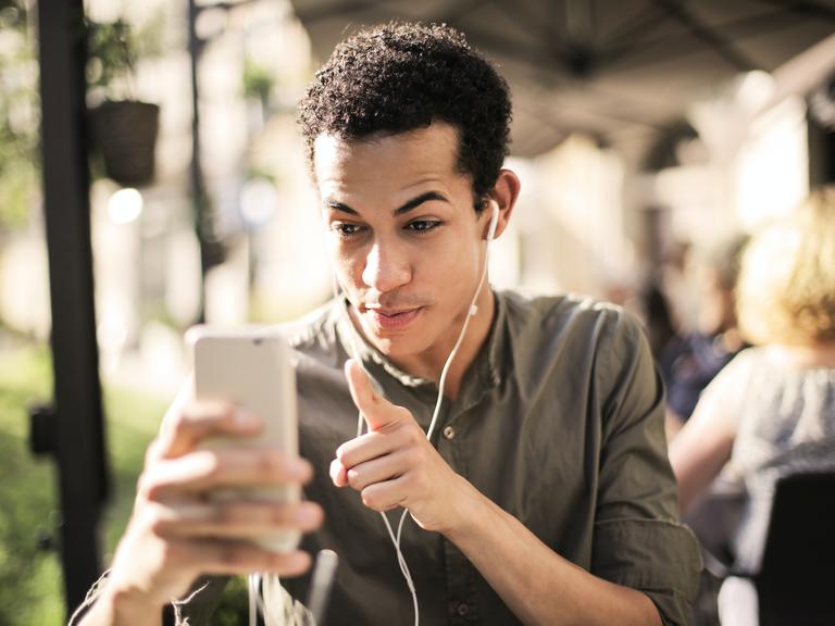 ein Mann mit Kopfhörern im Ohr macht einen Video mit dem Smartphone