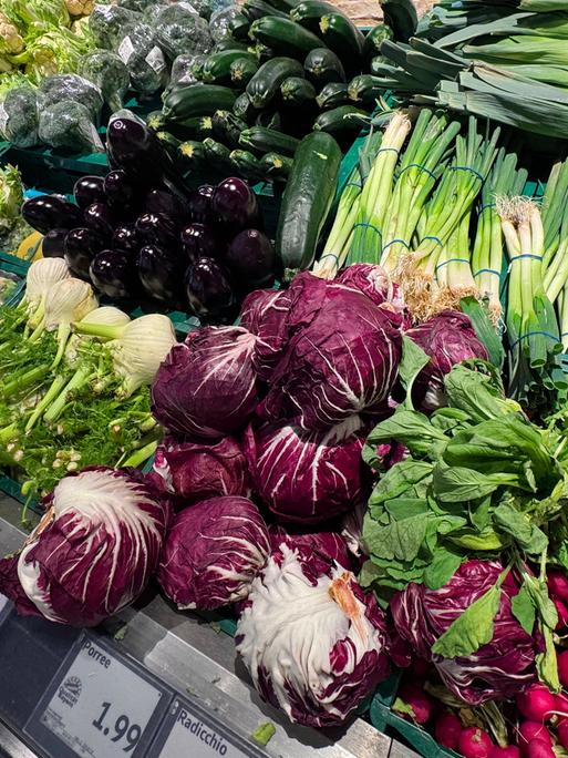 In der Gemüseabteilung eines Supermarkts sind verschiedene Gemüsesorten ausgelegt. Darunter sind Lauchzwiebeln, Fenchel und Radicchio.