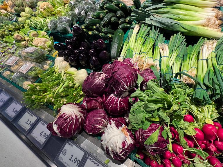 In der Gemüseabteilung eines Supermarkts sind verschiedene Gemüsesorten ausgelegt. Darunter sind Lauchzwiebeln, Fenchel und Radicchio.